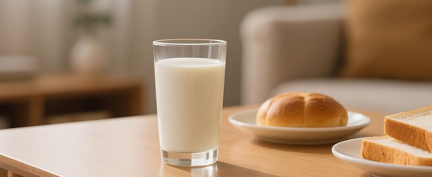 Glass of white milk and bread roll on wooden table with soft lighting and neutral background.