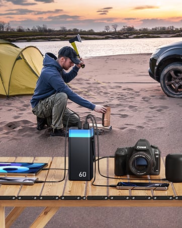 Photography equipment setup on beach at sunset, including camera, power bank, and yellow tent in background.