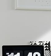 Close-up of a black digital device with a segmented display, positioned on a white surface near a wall.