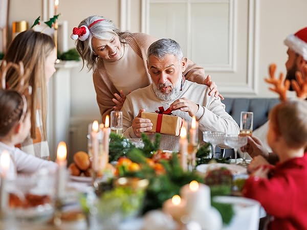 Family gathered around a festive dinner table with candles and decorations, opening gifts during a holiday celebration.