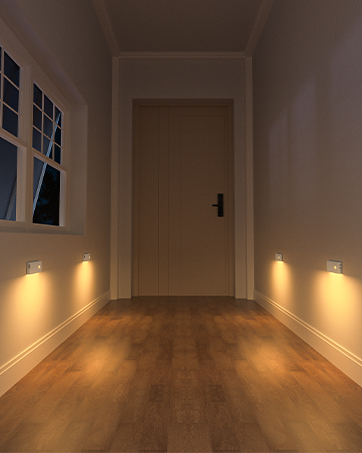Hallway with wooden flooring featuring wall-mounted lights on both sides, leading to a white door. Ambient lighting creates warm illumination.