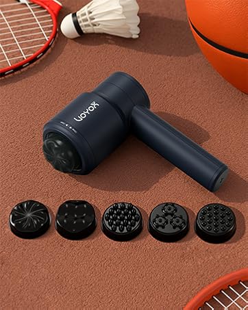 Black handheld massage gun with 5 different attachment heads displayed on brown surface alongside sports equipment.