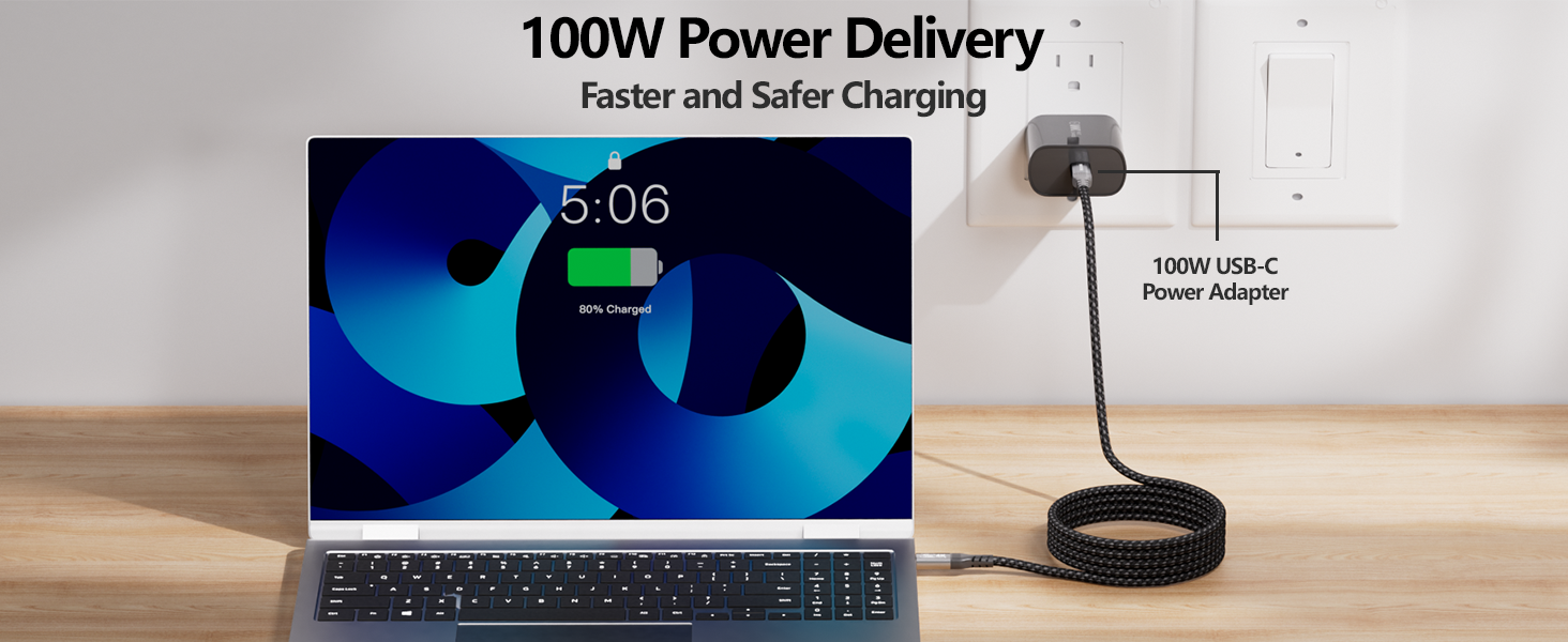 Text reads '100W Power Delivery'. Laptop displaying blue screen showing '5:06' with charging device or dock visible in foreground on wooden surface.