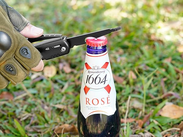 Gloved hand using bottle opener on a 1664 Rosé beer bottle in an outdoor grassy setting.