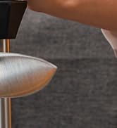 Close-up of a silver metallic surface, possibly part of a furniture or appliance, contrasting with a darker textured background.