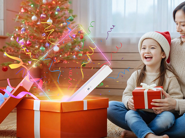 Red gift box with white ribbon opening to reveal bright golden light and colorful confetti explosion, positioned in front of a decorated Christmas tree.