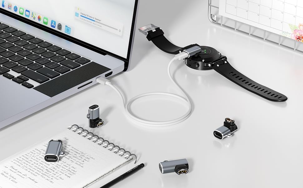 Collection of small USB adapters and charging cables arranged on a white desk surface alongside a laptop and smartwatch.