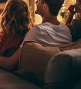 Dark indoor scene showing the back of two people sitting on what appears to be a couch or sofa.