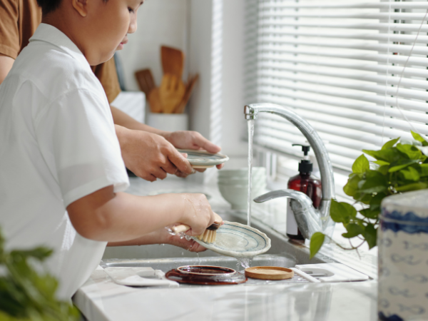 child cleaning the dishes at the sink with running water