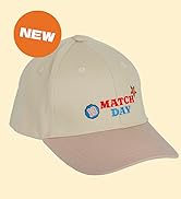 Text reads 'NEW' on orange circle badge and 'MATCH DAY' logo on cap. Light gray baseball cap with mauve bill, structured six-panel construction, curved visor.