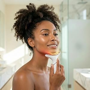 Woman using LED skincare device on jawline in bright modern bathroom