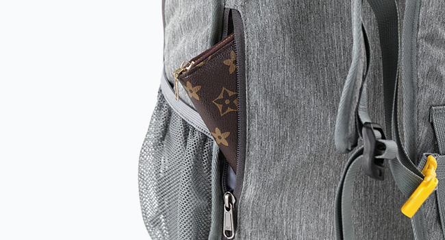 Close-up of a gray backpack with multiple compartments, showing a zipper pocket and a glimpse of a patterned item inside. Yellow zipper pull visible.