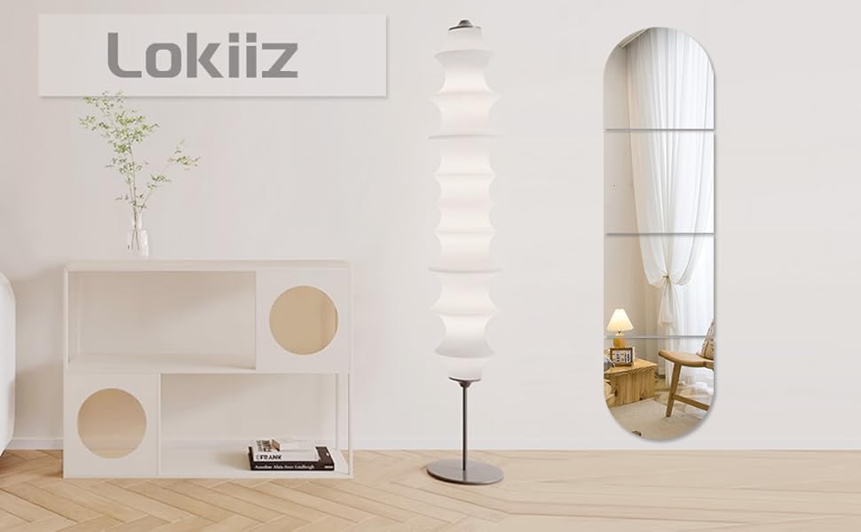 Minimalist interior with white walls, featuring a geometric wood structure with circular cutouts, arched mirror, floor lamp, and potted plant.