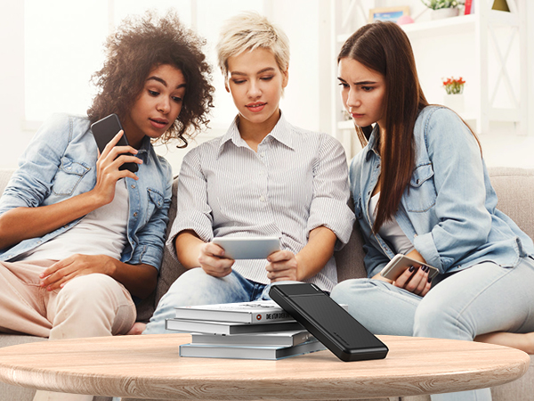 three women sitting on a couch looking at a tablet