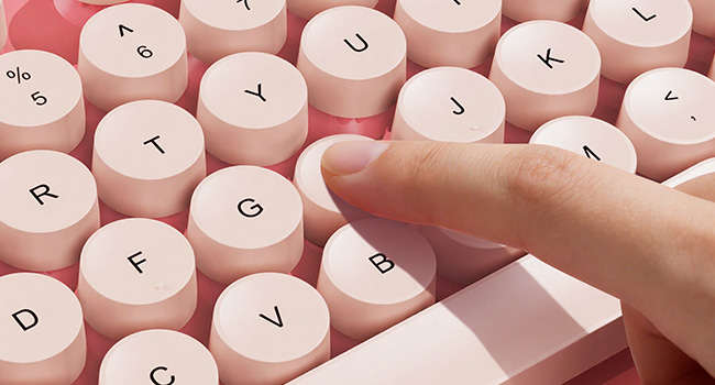 Finger pressing pink round keycaps on wireless keyboard for smooth responsive typing feel