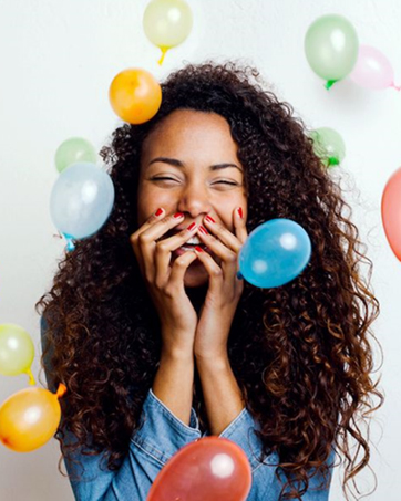 Black woman smiling and surrounded by colorful balloons