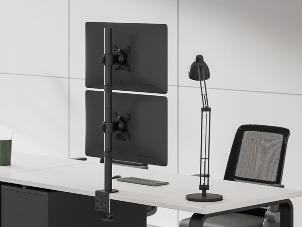 Dual monitor desk mount with vertical alignment, shown alongside a desk lamp and mesh office chair in a modern workspace setting.