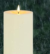Tall cylindrical cream-colored pillar candle with lit wick against dark green textured background.