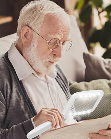 An elderly person using a handheld magnifying glass with built-in light to read a document while sitting on a couch.