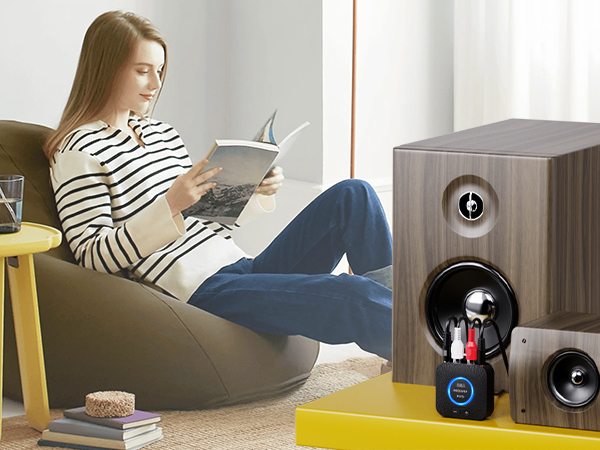 Living room scene with wooden speaker system featuring multiple drivers on the right, and comfortable seating area with yellow side table on the left.