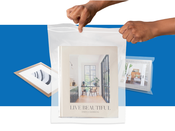 A pair of hands zip a bag shut with a book inside. Another book and picture frame lay behind it.