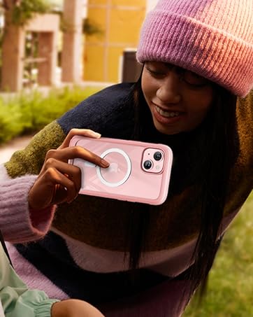 Two people using a pink smartphone to take a picture. One person is seated in a car with headphones, while the other leans in from outside.