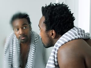 Man with a towel around his neck looking at his face in a foggy bathroom mirror.