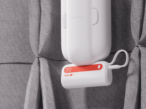 A white electronic device with red accents mounted on grey fabric. The device appears to be a sensor or monitoring unit with a cylindrical design.