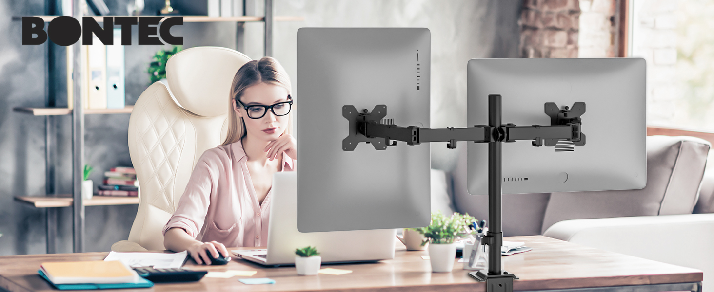 Dual monitor arm holding two screens, attached to a desk. Person working at computer workstation with keyboard and mouse.