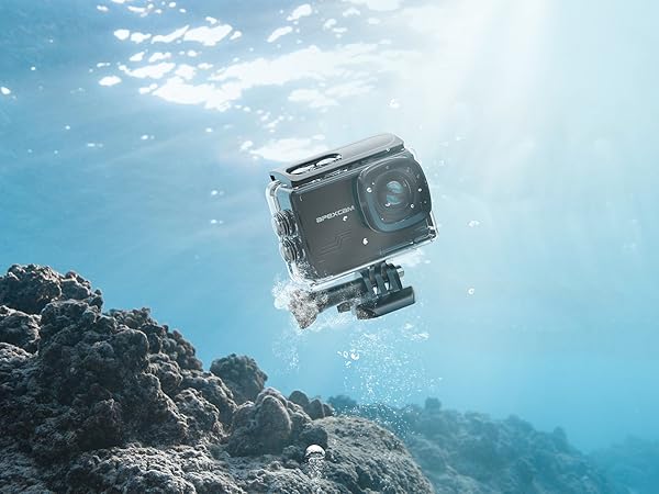 Waterproof action camera underwater, mounted on coral reef. Black rectangular device with lens visible, surrounded by bubbles in clear blue water.