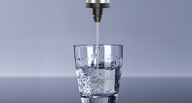 Clear glass filled with water, metal faucet pouring liquid from above. Droplets and splashes visible in the glass.