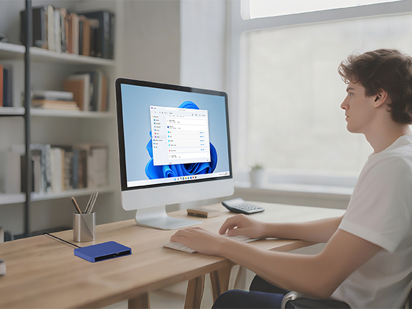 Person working at computer desk with monitor, shown from side angle in well-lit office environment.