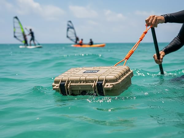 Waterproof case being pulled through turquoise ocean water, with windsurfers visible in the background.