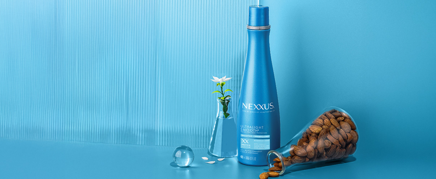 Nexxus bottle between a flower in a vase with water and a spilled lab glass filled with ingredients.