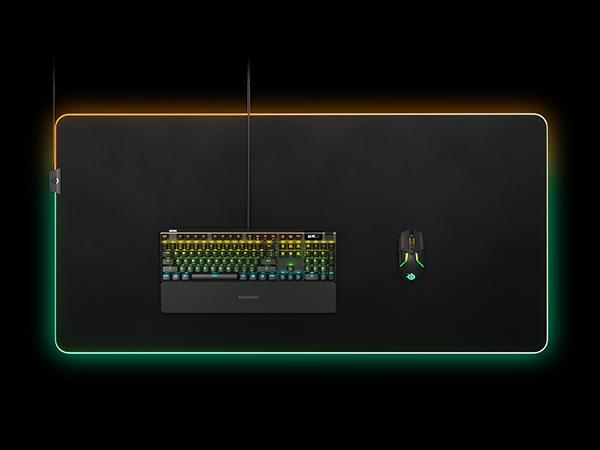 -SteelSeries QcK Prism 3XL mousepad with an Apex keyboard laying flat on a dark surface