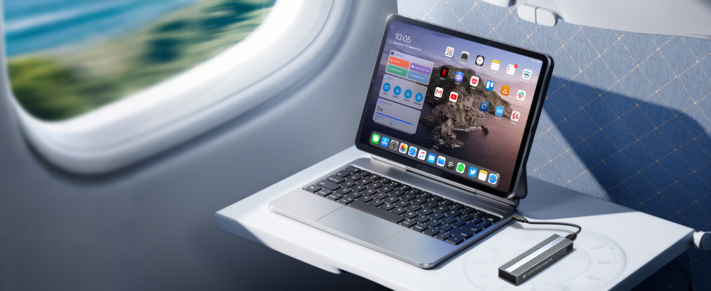 Tablet device with keyboard attachment on laptop-like stand, displaying colorful app icons. Positioned on tray table in airplane cabin with window visible.