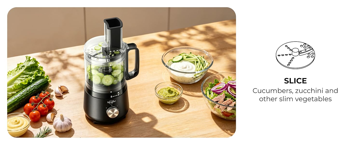 Mini food processor slicing cucumbers beside fresh produce, dips and a prepared salad