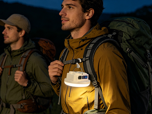 Two hikers walking at night with a portable LED camping lantern clipped to a backpack