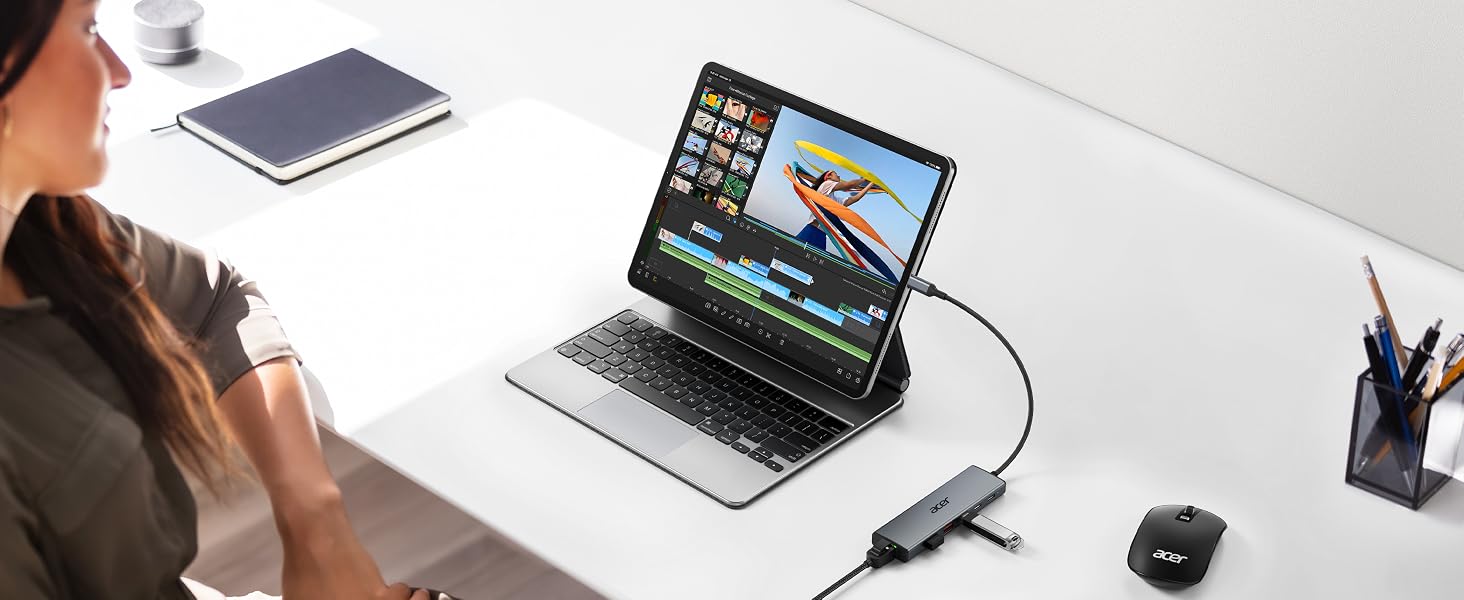 Overhead workspace setup showing laptop with external display connected via cable, tablet, smartphone, desk organizer, and other accessories on white surface, demonstrating multi-device connectivity.