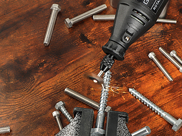 Power drill in use on wooden surface, surrounded by various metal screws and bolts. Drill is creating metal shavings as it operates.