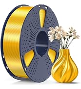 3D printer filament spool with gold-colored filament on gray perforated holder, next to a matching gold spiral-patterned vase containing white flowers.