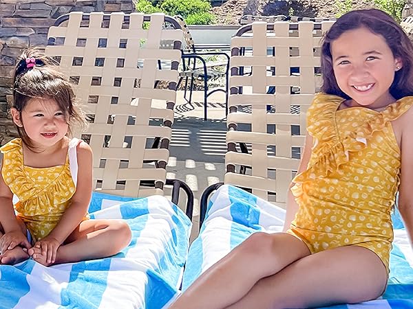 Little girls in summer clothes, smiling while sitting on beach towels