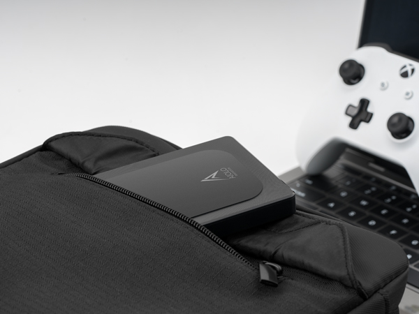 Portable charger on laptop next to gaming controller. Black rectangular power bank sits on keyboard, with white controller visible in upper right corner.