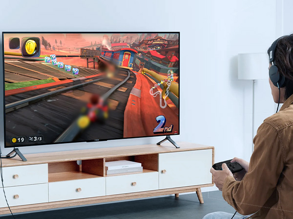 Gaming setup showing TV mounted above white media console, displaying racing game graphics with person visible in viewing position.