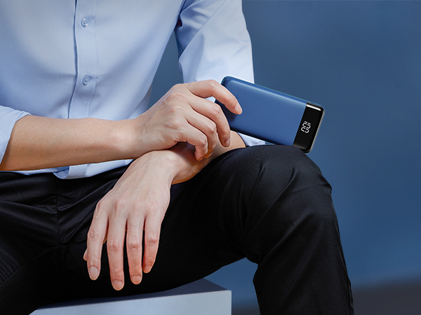 Person in blue shirt holding a blue rectangular device with a small digital display, possibly a power bank or portable charger.