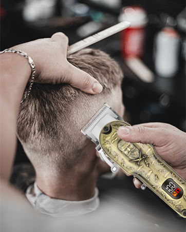Close-up of a haircut in progress. A hand holds a decorative electric hair clipper with a gold design against the back of a person's head.