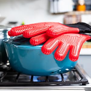 Red silicone gloves placed on a cooking pot showing heat resistance on stovetop.