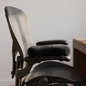 Black armrest pad on mesh office chair beside wood desk.