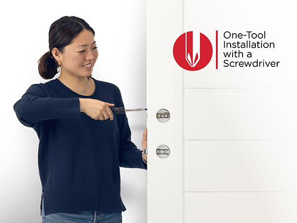 A smiling woman screwing in a door latch with a screwdriver.