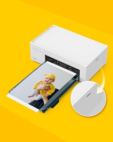 Compact white photo printer on yellow background, printing image of baby. Printer has minimalist design with rounded edges.